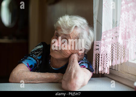 Una donna anziana siede pensieroso al tavolo. Foto Stock
