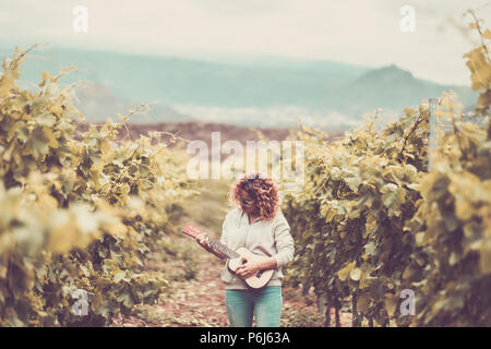 Bella bella donna caucasica camminare da soli nella vigna sfondo verde cantando un ukulele chitarra acustica. libertà uno stile di vita alternativo hippy con Foto Stock