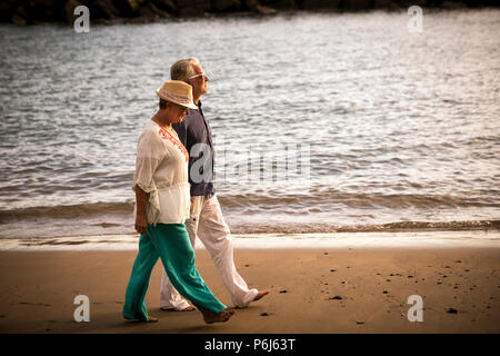 Senior adulto giovane camminare insieme sulla riva con vista oceano in background. Godetevi le attività per il tempo libero tempo rilassato. In eterno amore intramontabile concetto in sc Foto Stock