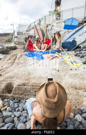 Il gruppo di donne giovani amici stare insieme sulla costa in estate divertimento e sorrisi. Uno di loro di scattare foto agli altri usando una tecnologia sma Foto Stock