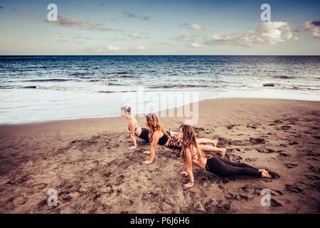 Tre cacuasian giovani donne facendo pilates sulla riva vicino alle onde e l'oceano. outdoor le attività per il tempo libero sport e stile di vita per il fitness beauti Foto Stock