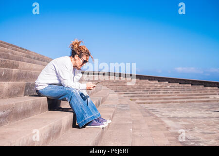 Lonely medioevo Donna al lavoro con uno smartphone seduto su una lunga e bellissima staris in concorso urbano. Tempo libero con tehnology concetto per la donna moderna Foto Stock