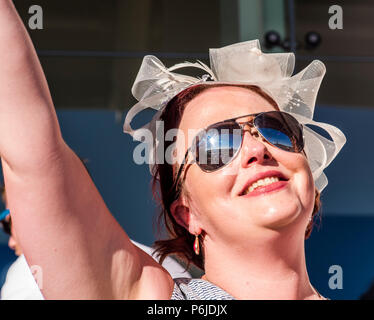 Gara femminile goer indossando fascinator e occhiali da sole, cantare insieme a un Paloma fede canzone con York Racecourse si riflette nei suoi occhiali, York, Inghilterra, 30 giugno 2018 Foto Stock