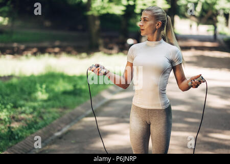 Ritratto di montare la giovane donna con salto con la corda nel parco. Femmina Fitness facendo allenamento all'aperto nel parco sulla giornata di sole. Foto Stock