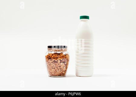 Muesli fatti in casa in un barattolo di vetro legate corda di iuta accanto alla bottiglia di latte su sfondo bianco. Gli ingredienti di una sana colazione composizione minima. Foto Stock