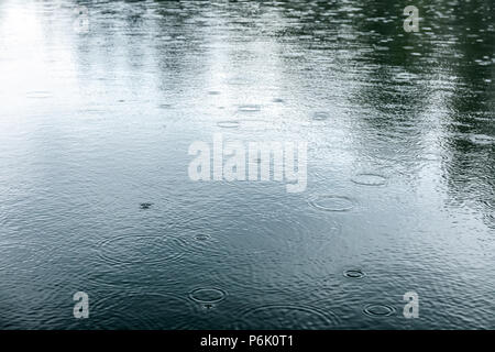 Gocce di pioggia di increspatura sulla superficie del lago con alberi circostanti riflessioni Foto Stock