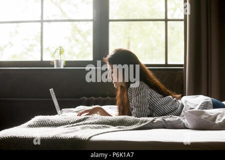 Felice ragazza sorridente mentre texting al ragazzo al laptop Foto Stock