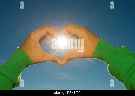 Donna di mani creare forma di cuore contro il sole e cielo blu in Ticino, Svizzera. Foto Stock