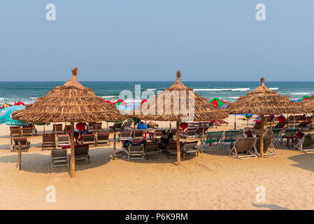 Da Nang, Vietnam--marzo 23, 2016. Sun bagnanti rilassarsi sulle sedie a sdraio sotto il tetto di paglia ombrelloni sulla spiaggia in Cina. Foto Stock