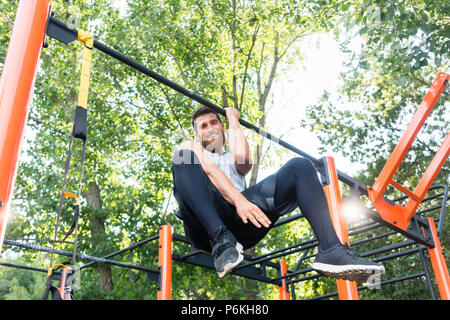 Potente giovane uomo che fa un braccio-pull-up mentre è appesa su una barra Foto Stock
