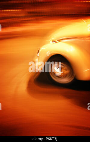 In rapido movimento di VW Beetle auto a guidare di notte attraverso la nightmarket a Chiang Mai, Thailandia Foto Stock