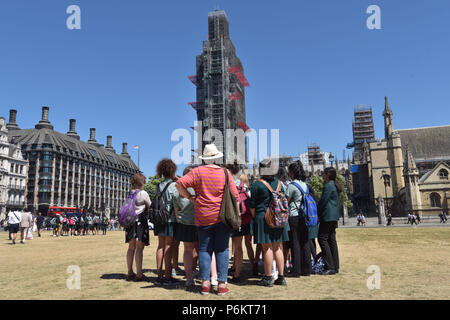 I turisti ed i visitatori di Londra si riuniscono in gruppi in Westminster fuori le case del Parlamento dove il Big Ben è coperto di impalcatura come subisce Foto Stock