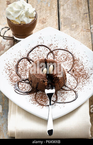 Dolce al cioccolato torta decorata con lo sciroppo al cioccolato mandorle e cacao in polvere e la tazza di caffè espresso con panna montata su legno tavolo rustico Foto Stock