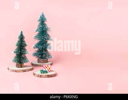 Albero albero di Natale sul registro di legno fetta con la presente casella sul rosa pastello di sfondo per studio.vacanza festosa celebrazione biglietto di auguri con copia spazio per Foto Stock