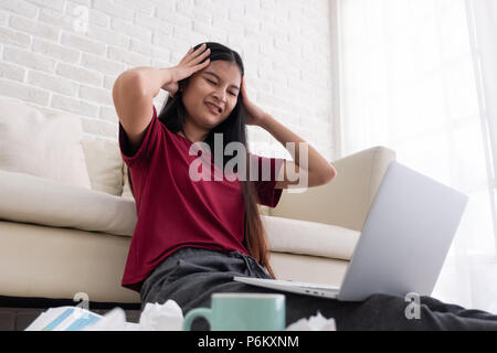 Donna asiatica del freelancer emozioni stress mentre si lavora con il computer portatile e documenti cartacei al divano nel soggiorno in casa.Il lavoro a casa concept Foto Stock