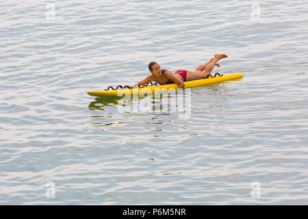 Bournemouth Dorset, Regno Unito. Il 1 luglio 2018. Regno Unito: meteo sole nebuloso, ma ancora caldo come migliaia di testa sunseekers per le spiagge di Bournemouth per godere di una giornata al mare. Femmina bagnino RNLI sulla tavola da surf. Credito: Carolyn Jenkins/Alamy Live News Foto Stock