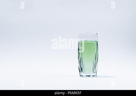 Sfaccettata in vetro riempita con il verde di liquido trasparente si erge su uno sfondo bianco. Composizione minima della bevanda rinfrescante con copia spazio. Foto Stock