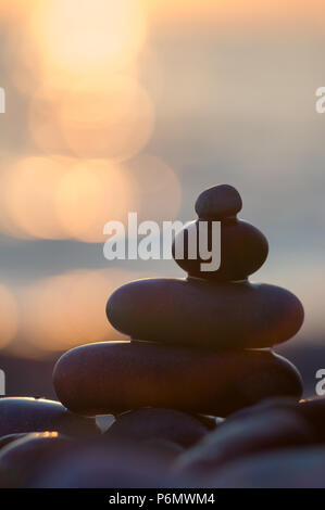 Piramide piegata Zen pietre ghiaia sul mare spiaggia al tramonto Foto Stock