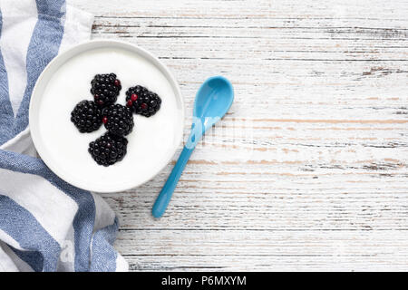 Yogurt con frutti di bosco in un recipiente su sfondo di legno. Vista superiore, copia spazio per il testo Foto Stock