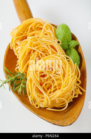 Fasci di spaghetti e le erbe in un cucchiaio di legno Foto Stock