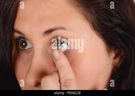 Primo piano della faccia femmina con applicazione di lente a contatto sui suoi occhi marroni. Oftalmologia medicina concetto. Foto Stock