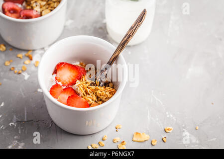 Muesli fatti in casa di cocco con yogurt e frutti di bosco in piccole ciotole di bianco. Cibo sano concetto. Foto Stock