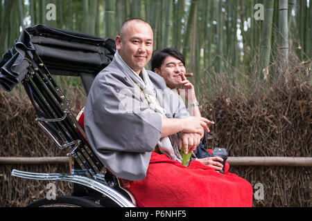 Turisti giapponesi che fumano sigari in un rickshaw tradizionale tirato a mano nella Foresta di Bamboo di Sagano ad Arashiyama alla periferia di Kyoto, Giappone. Foto Stock