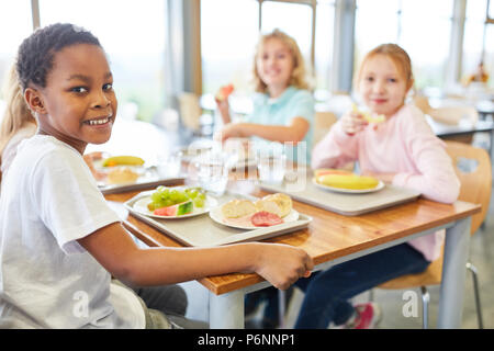 I bambini mangiano insieme nella mensa del multiculturale della scuola elementare Foto Stock