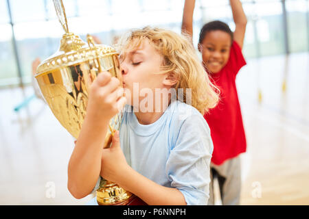 Felice ragazzo baci una tazza dopo un concorso in educazione fisica Foto Stock