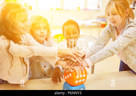 Felice gruppo di bambini è mani di impilamento in scuola come concetto di lavoro di squadra Foto Stock