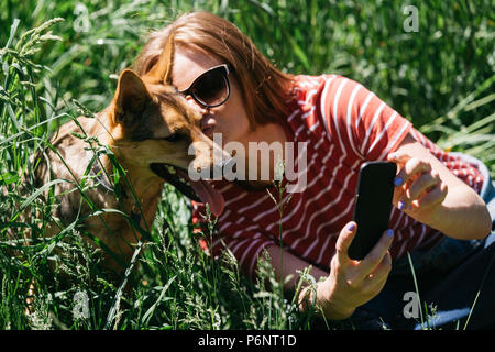 Immagine della donna facendo selfie sulla passeggiata con il cane sul prato verde Foto Stock