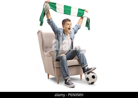 Overjoyed teenage tifoso di calcio con una sciarpa e un campo di calcio seduto in poltrona isolati su sfondo bianco Foto Stock