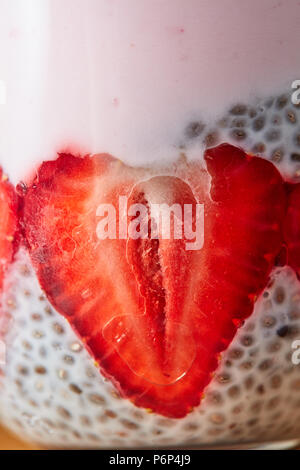 Un maturo la metà delle fragole con yogurt e organici semi di chia in un vetro trasparente. Foto macro Foto Stock