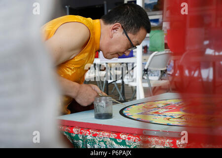 Monaco tibetano opere attentamente su un coloratissimo Mandala di sabbia. Foto Stock