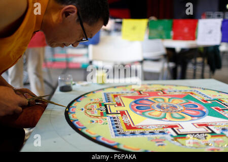 Monaco tibetano opere attentamente su un coloratissimo Mandala di sabbia. Foto Stock