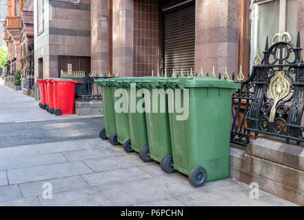 Una fila di 6 rosso e 5 verde scomparti wheelie sul marciapiede in una strada nel centro della città di Manchester, Regno Unito Foto Stock