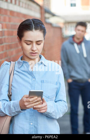 Giovane donna Texting per aiutare sul telefono cellulare pur essendo sgambate su strada di città Foto Stock