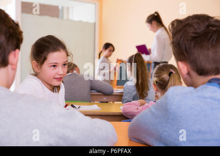 Felice di chattering alunni seduti sui banchi torna alla lezione di scuola elementare Foto Stock