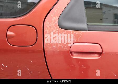 Sbiadita vernice auto - peeling superficiale di vernice in un 20 Anno europeo vecchia auto rossa. Foto Stock