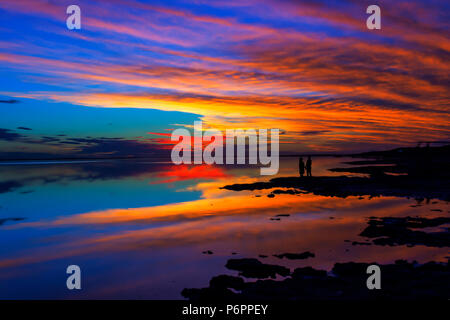 Colorato tramonto sul lago di Epecuen, in Carhue, Buenos Aires, Argentina. Silhouette di un cople tenendo le mani nel lago. Foto Stock