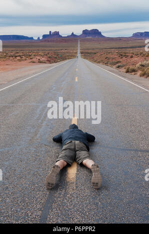 L'uomo che giace piatto su il suo ventre per scattare una foto della strada statale 163 che conduce alla Monument Valley, Arizona, Stati Uniti. Foto Stock