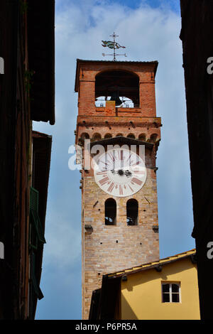 Lucca " medievale Torre delle Ore' (Torre dell'orologio), visto da una stretta strada in città il centro storico con il cielo nuvoloso Foto Stock