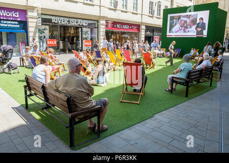 Bath, Regno Unito, 2 luglio, 2018. Come bagno gode di un altro molto calda e soleggiata giornata gli acquirenti sono ritratte godendo il sole in SouthGate shopping center dove un grande schermo è stato impostato in modo che gli appassionati di tennis possono guardare il torneo di Wimbledon Tennis Championship, forecasters prevedono che il clima caldo proseguirà anche nella prossima settimana. Foto Stock