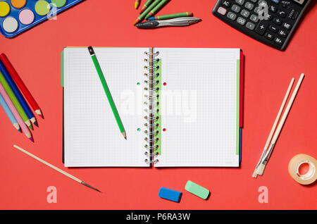 Blocco note e forniture scolastiche, articoli di cancelleria, sfondo rosso. Vuoto il blocco note per il tuo testo. Foto Stock