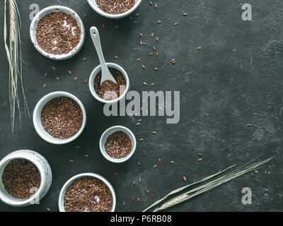 Semi di lino e di segale secco ear su sfondo scuro. Set di piccole ciotole con organici di semi di lino o semi di lino. Semi di lino è ricco in acido grasso omega-3. Copia Foto Stock