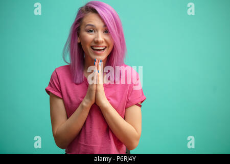 Positivo donna felice con taglio di capelli rosa mantiene le palme insieme, ringraziando il suo fidanzato per dono, isolate su blue studio dello sfondo. Felice adorabili youn Foto Stock