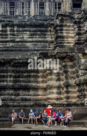 Turisti asiatici di riposo in un cortili in corrispondenza della base di un tempio di pietra arenaria a Angkor Wat, Siem Reap, Cambogia. Foto Stock