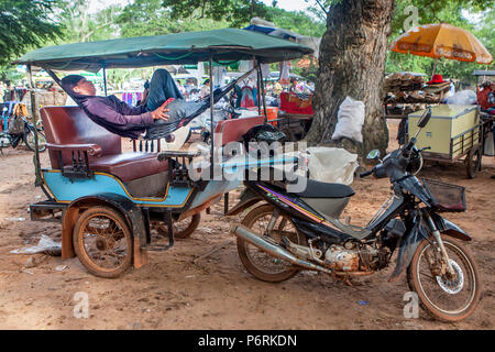 Un tuk tuk driver si rilassa nella sua amaca ascoltando la musica sul suo smartphone a Angkor Wat, Siem Reap, Cambogia. Foto Stock