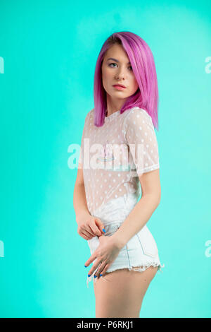 Elegante Attraente giovane donna con verniciato colorato capelli, figura snella. Mezza Lunghezza in piedi e guardando a parte. Isolato su sfondo blu. Foto Stock