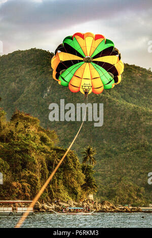 Il parasailing sulla spiaggia bianca con foreste tropicali montagne sullo sfondo a Puerto Galera, Oriental Mindoro, isola filippina Foto Stock